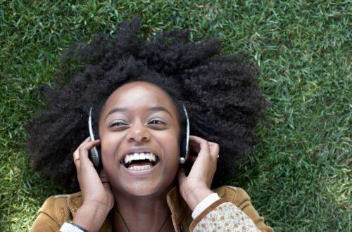 woman smiling in the grass while holding headphones over ears
