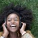 woman smiling in the grass while holding headphones over ears
